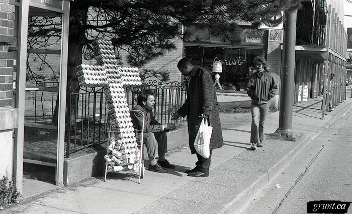 1993 04 06 Sculpture Public Works James Carl street performance Carl sitting beside road with beer can cross interacting with public